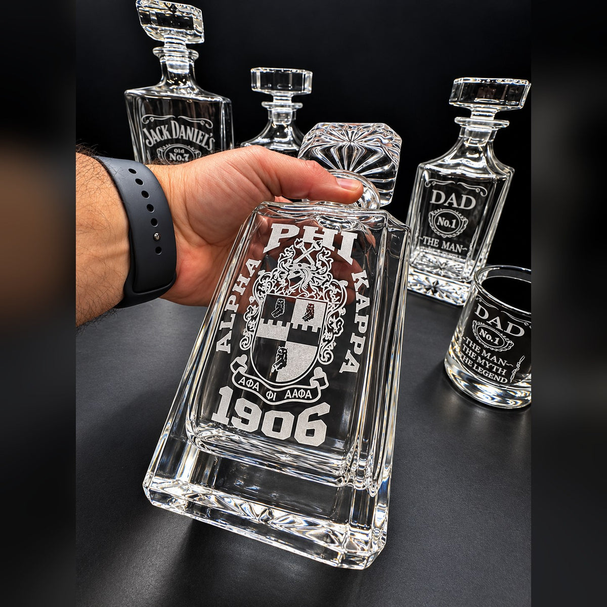 750 ml engraved square glass decanter held in hand, custom monogram crest with 1906 date, shown with engraved glasses