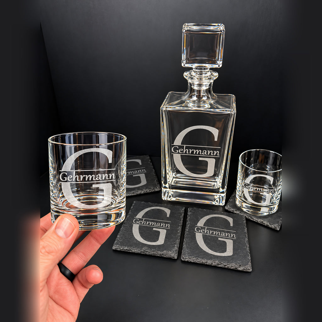 Engraved 810 ml whiskey decanter gift set with two monogrammed rocks glasses and four slate coasters, hand holding glass