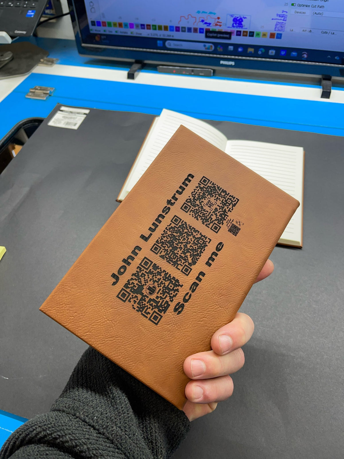 Hand holding a rawhide leatherette journal engraved with a name and QR codes