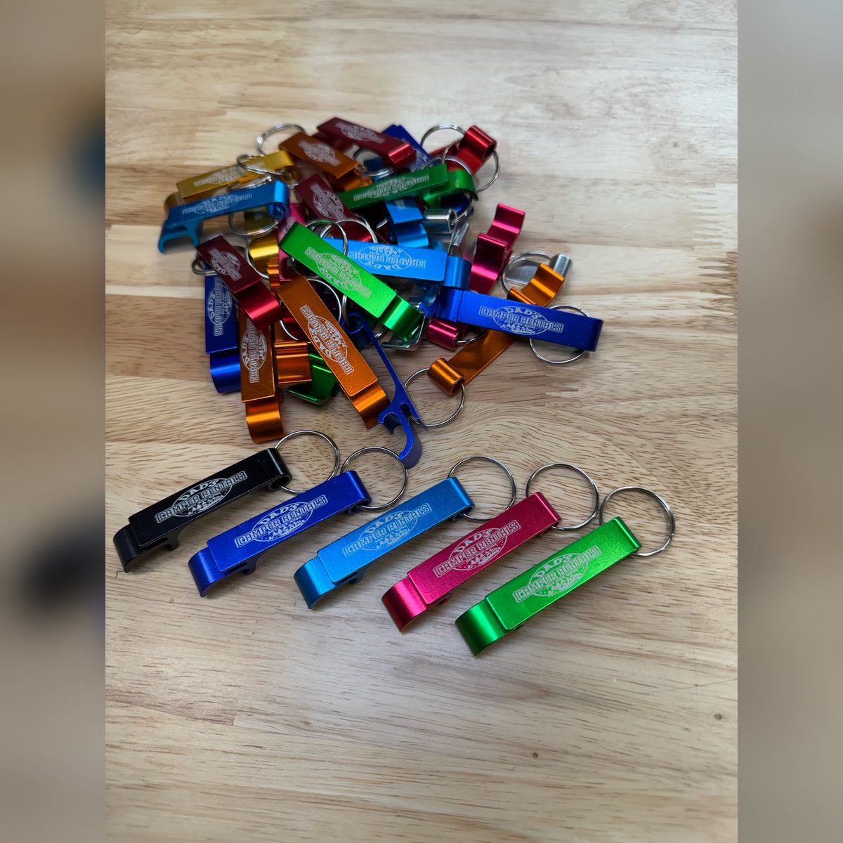 Pile of multicolor custom engraved metal bottle openers with keyrings, five laid out in front
