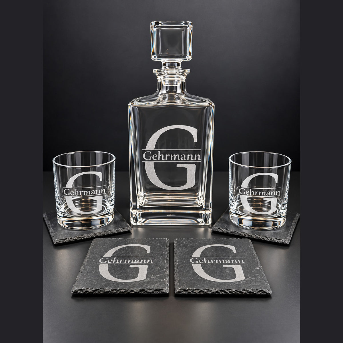 Engraved square glass decanter with stopper, two engraved rocks glasses, and engraved slate coasters